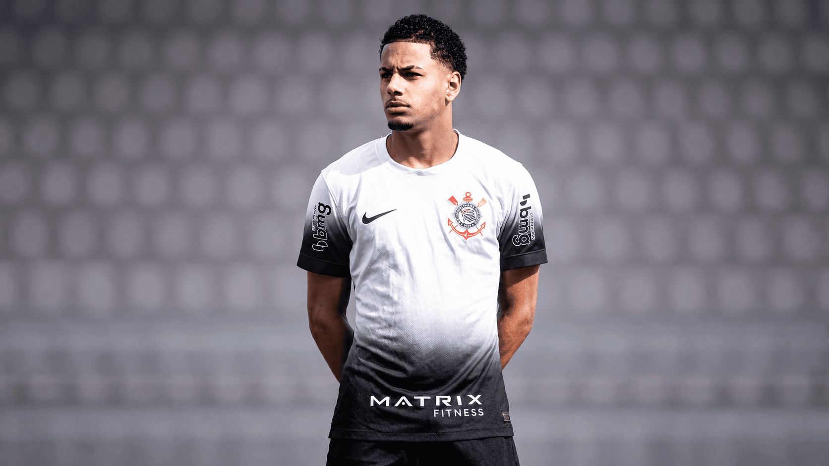 Denner, lateral-esquerdo revelado pelo Corinthians e contratado pelo Chelsea, posa com a camisa alvinegra diante de um fundo cinza desfocado.